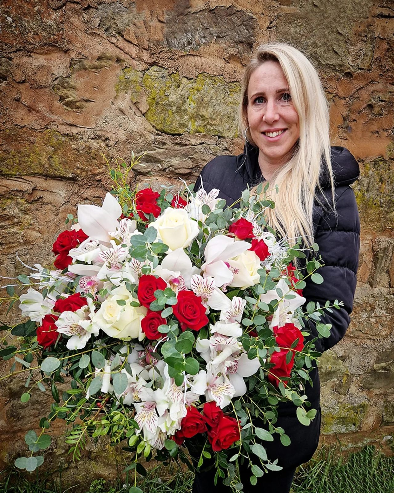 Martina Drexlerová drží velkou vázanou kytici z červených a bílých růží, orchidejí a eukalyptu